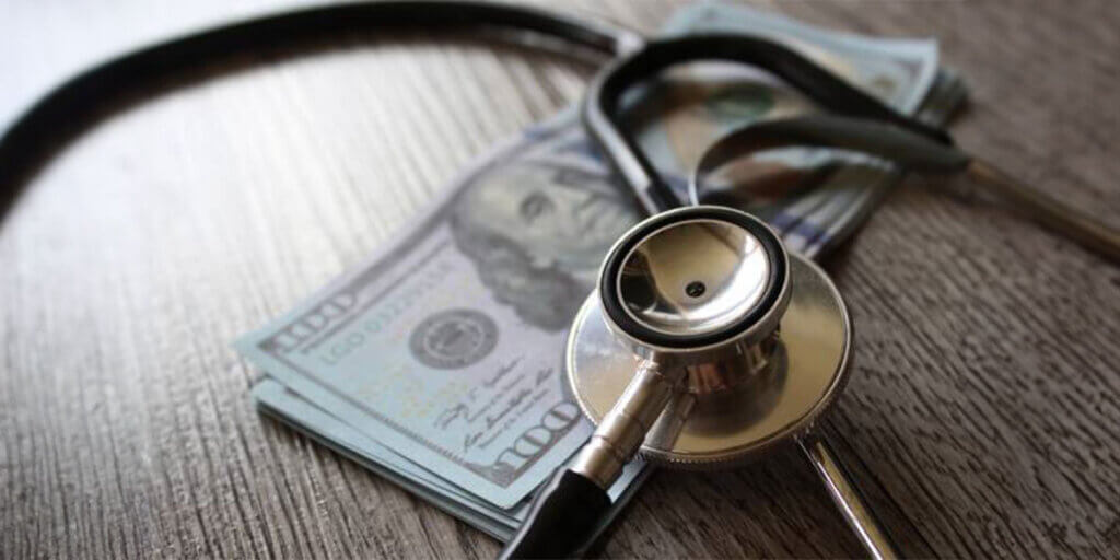 stethoscope rests on top of a stack of $100 bills