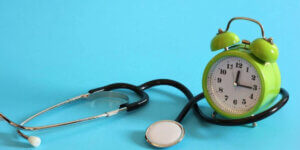A green alarm clock and stethoscope on a blue background.