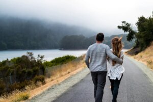 man and a woman walking together down an empty path by a lake on a misty day