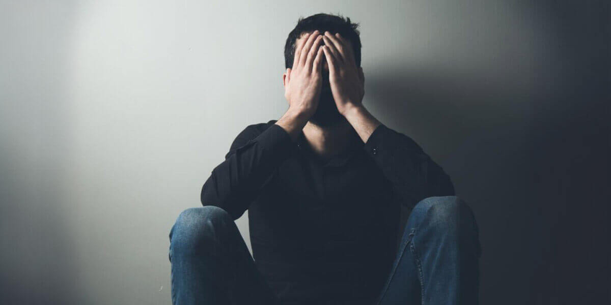 A man sitting on the floor, covering his face with his hands in a state of distress or frustration.