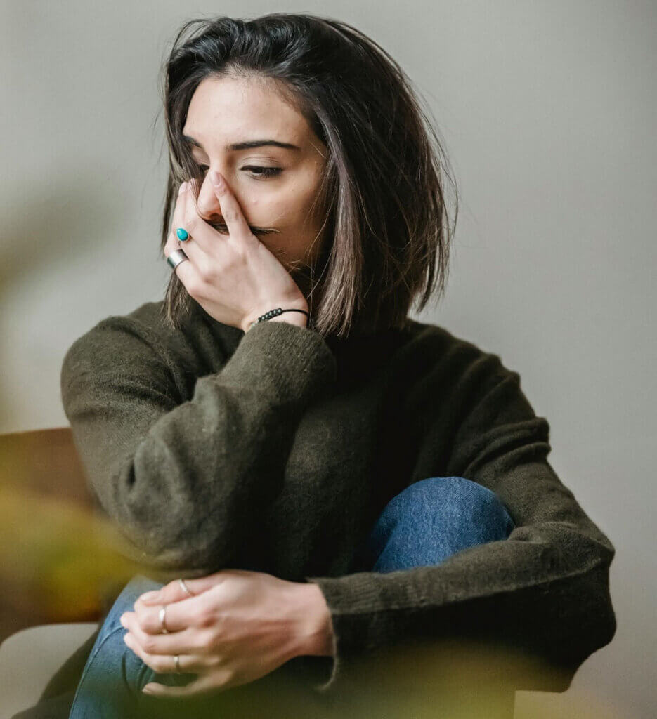 a woman sits with her hand covering her mouth, and looks away wistfully