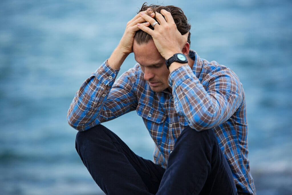 a man sits by the oceanside and puts his hands on his head