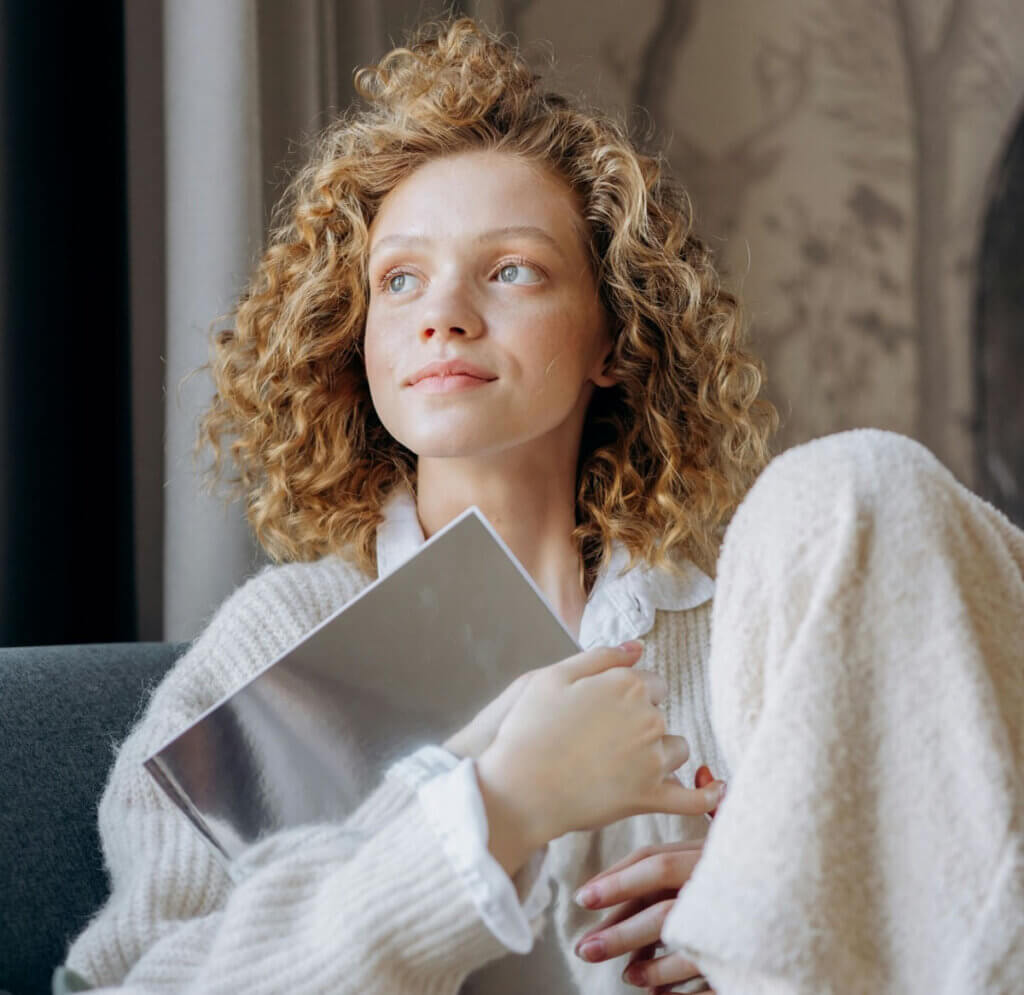 a woman sits on a couch in cozy clothes and looks towards the light