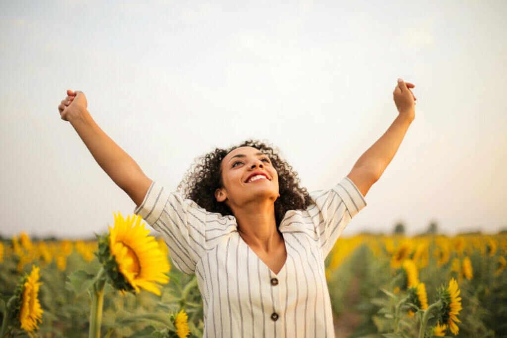 a woman stands in a sunflower field, smiling with her arms outstretched