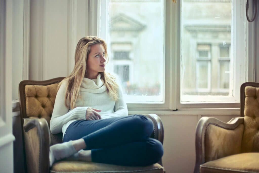 a woman sits on a chair and looks out the window