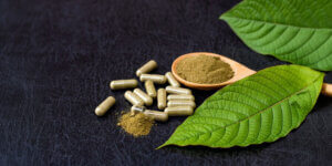 Kratom leaf and capsules on a black table.