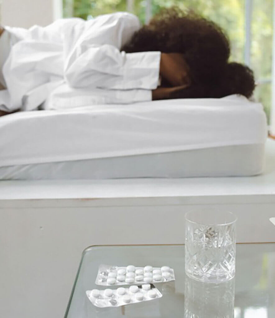 A person sleeping on a bed next to a pack of pills and a glass of water.