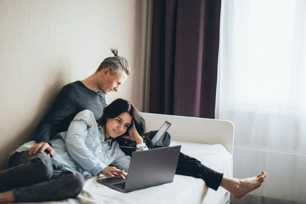 A woman and a man relaxing on a bed with their laptops.