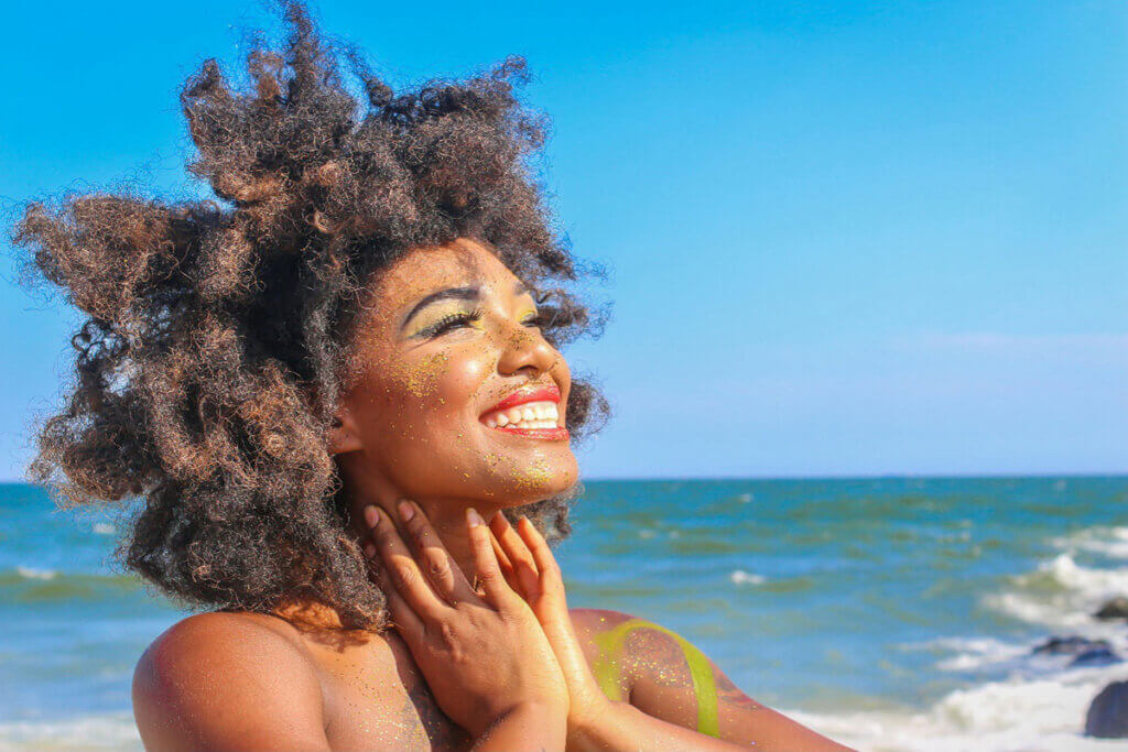 A woman with curly hair smiling at the beach.