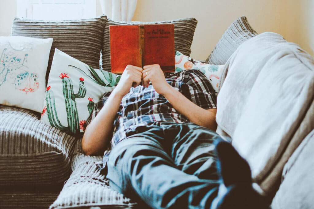A man sits comfortably on a couch, engrossed in reading a book, surrounded by a cozy atmosphere.