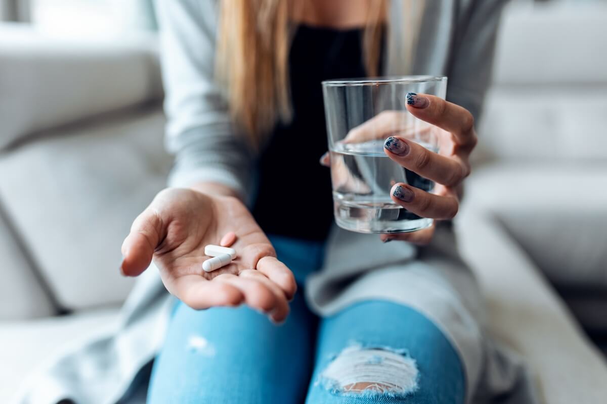 Young woman taking pills while holding glass of water sitting on