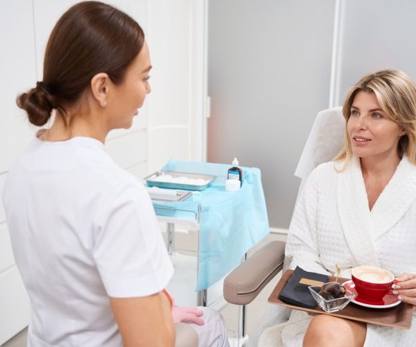 Doctor cosmetologist consults a woman in a clinic of aesthetic medicine, the patient is comfortably seated with tea and fruits